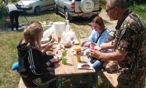 trzy osoby siedzą przy stole, mężczyzna podaje im picie