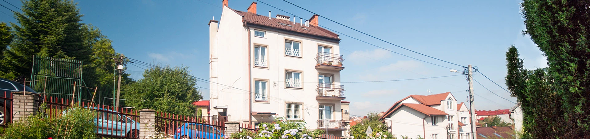 Widok na ogród z kwitnącymi różami, w tle budynki mieszkalne.