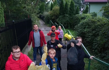 grupka dzieci z wychowawcami niosą worki ze śmieciami