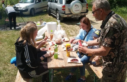 trzy osoby siedzą przy stole, mężczyzna podaje im picie